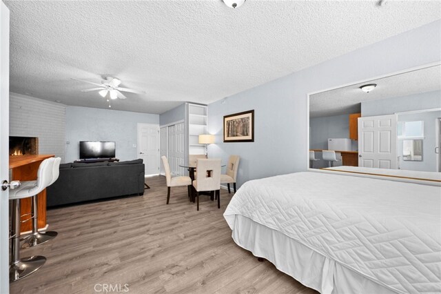 bedroom with ceiling fan, light hardwood / wood-style floors, a textured ceiling, and a brick fireplace