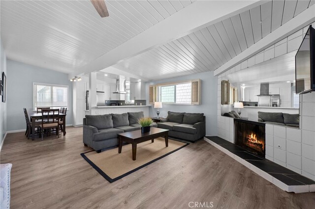 living room featuring ceiling fan, a fireplace, lofted ceiling with beams, and wood-type flooring
