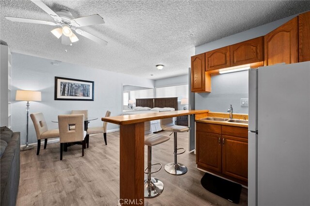 kitchen featuring a textured ceiling, light wood-type flooring, white fridge, and sink