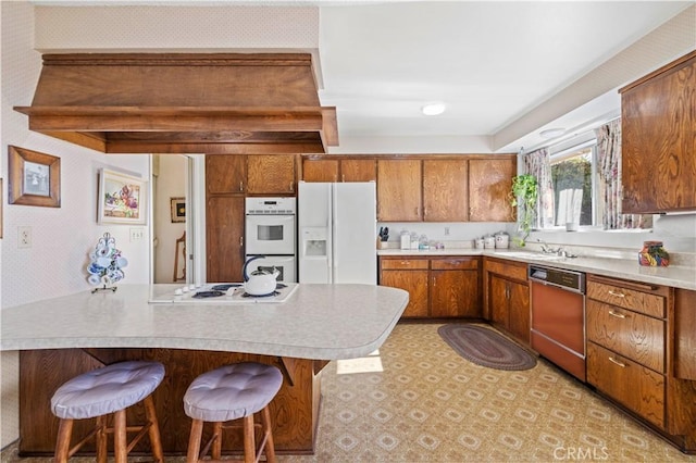 kitchen with kitchen peninsula, sink, white appliances, and a breakfast bar area