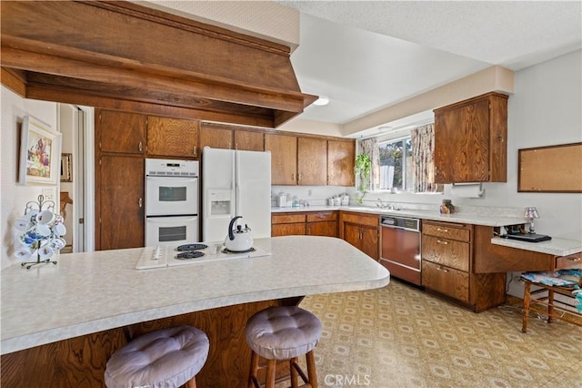 kitchen featuring white appliances, kitchen peninsula, and a kitchen bar