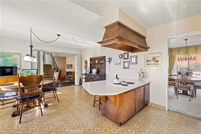 kitchen with custom exhaust hood, white cooktop, kitchen peninsula, decorative light fixtures, and a notable chandelier