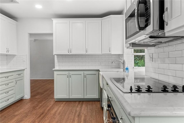 kitchen featuring sink, backsplash, wood-type flooring, and white cabinets