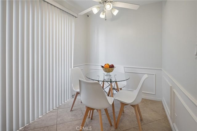 tiled dining area with a decorative wall, a ceiling fan, and a wainscoted wall