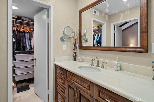 bathroom with vanity, a spacious closet, a textured wall, and visible vents