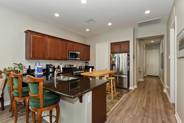 kitchen with dark stone countertops, sink, light wood-type flooring, appliances with stainless steel finishes, and a kitchen breakfast bar