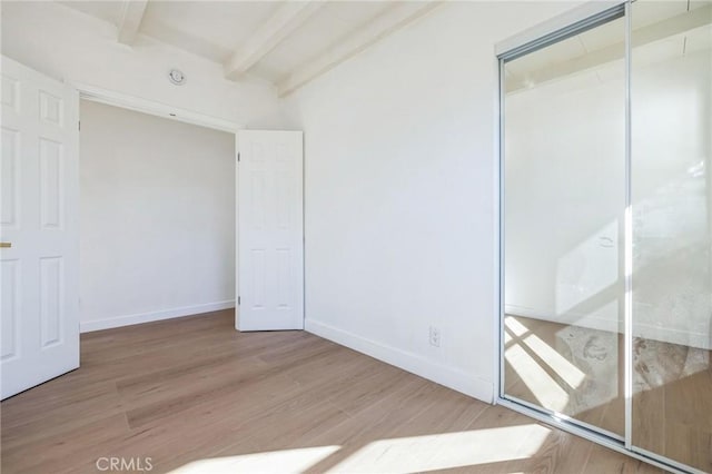 unfurnished bedroom with hardwood / wood-style flooring, a closet, and beamed ceiling