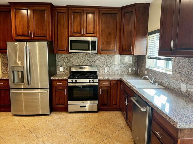 kitchen with sink, decorative backsplash, light tile patterned flooring, light stone counters, and stainless steel appliances