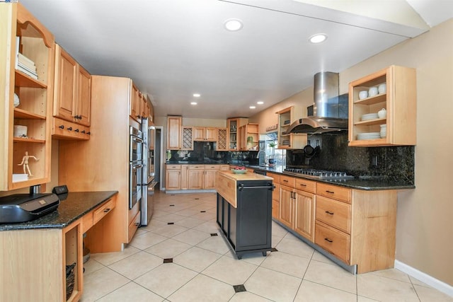 kitchen featuring light tile patterned floors, appliances with stainless steel finishes, dark stone counters, wall chimney range hood, and a kitchen island