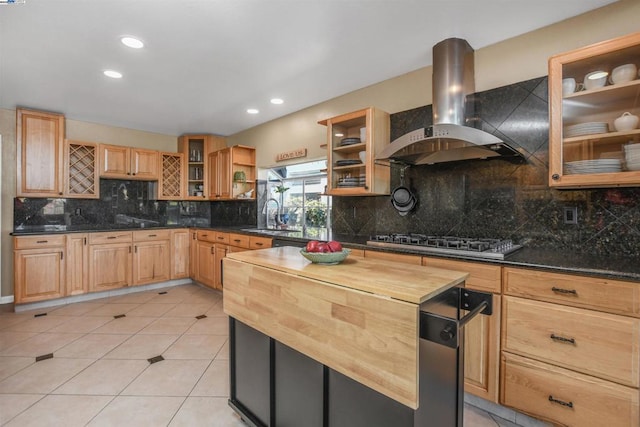 kitchen with tasteful backsplash, wooden counters, wall chimney range hood, light tile patterned flooring, and stainless steel gas cooktop