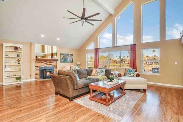 living room featuring ceiling fan, a high ceiling, light hardwood / wood-style flooring, a wood stove, and built in shelves