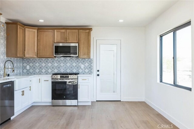 kitchen with white cabinetry, light hardwood / wood-style floors, appliances with stainless steel finishes, backsplash, and sink