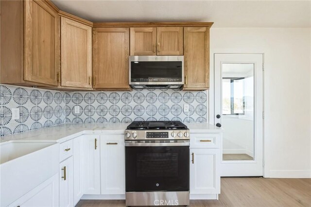 kitchen featuring backsplash, stainless steel appliances, light stone counters, white cabinets, and light wood-type flooring