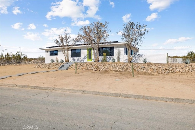 view of front of house featuring roof mounted solar panels and fence