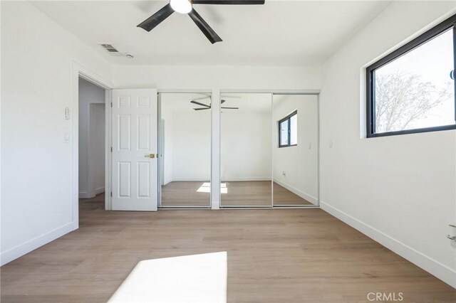 unfurnished bedroom with ceiling fan, two closets, multiple windows, and light wood-type flooring