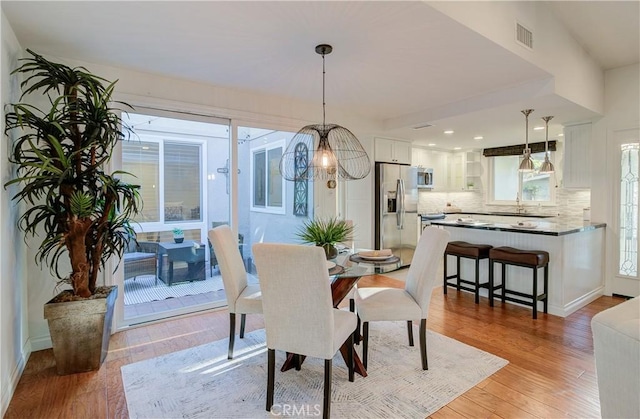 dining room with light wood-type flooring, a notable chandelier, and sink