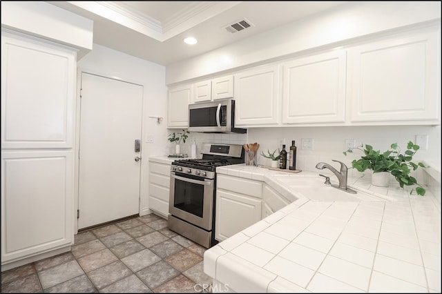 kitchen featuring white cabinets, stainless steel appliances, sink, tile countertops, and crown molding