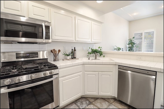 kitchen with sink, stainless steel appliances, white cabinetry, and tile countertops