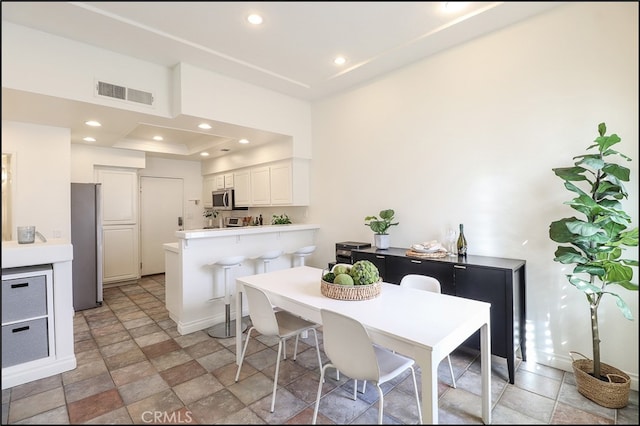 kitchen featuring a kitchen breakfast bar, white cabinets, kitchen peninsula, stainless steel appliances, and a tray ceiling