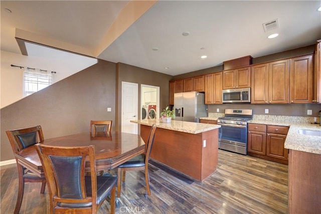 kitchen featuring dark wood-type flooring, separate washer and dryer, a kitchen island, stainless steel appliances, and light stone countertops