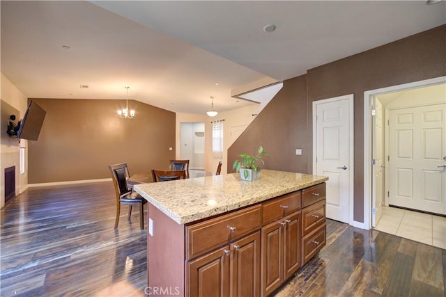 kitchen with decorative light fixtures, a chandelier, a center island, light stone counters, and dark wood-type flooring