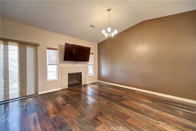 unfurnished living room with lofted ceiling, hardwood / wood-style floors, a tile fireplace, and a notable chandelier