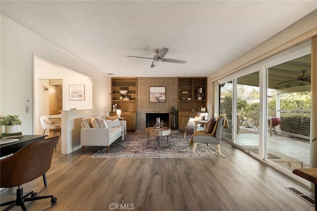 living room with hardwood / wood-style flooring, ceiling fan, a fireplace, built in features, and a textured ceiling