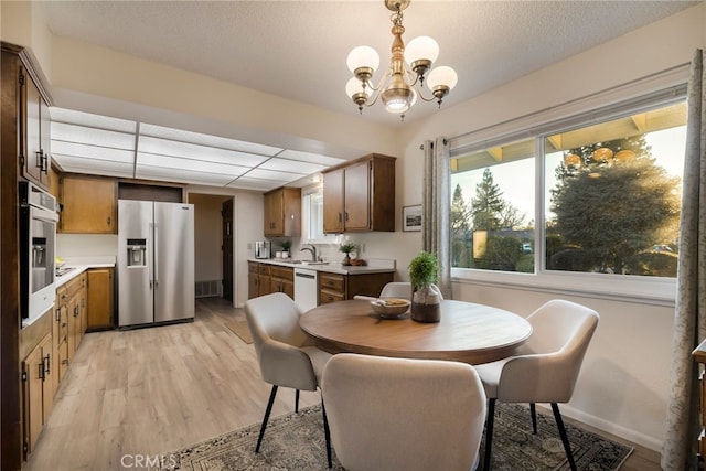 dining area with sink, a textured ceiling, light hardwood / wood-style flooring, and a chandelier