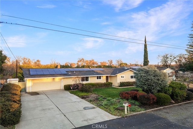 ranch-style home with a garage, a front yard, and solar panels