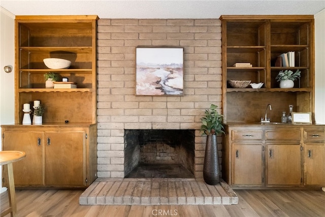 living room with a brick fireplace, sink, and light wood-type flooring