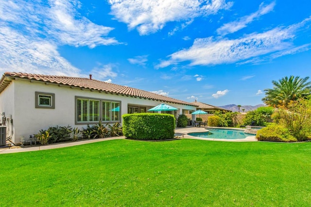 back of property featuring a swimming pool with hot tub, a mountain view, central AC unit, a yard, and a patio