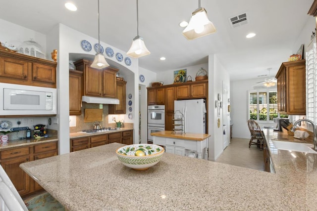 kitchen with tasteful backsplash, sink, white appliances, hanging light fixtures, and a kitchen breakfast bar