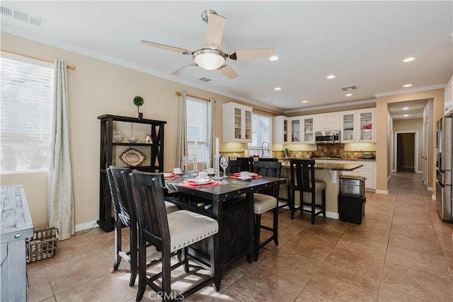 dining space featuring ceiling fan, light tile patterned floors, sink, and ornamental molding