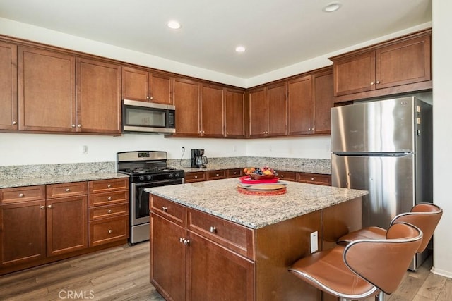 kitchen with wood-type flooring, appliances with stainless steel finishes, a center island, and light stone counters