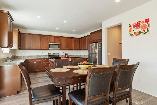 kitchen with sink, stainless steel appliances, light hardwood / wood-style floors, light stone countertops, and a kitchen island