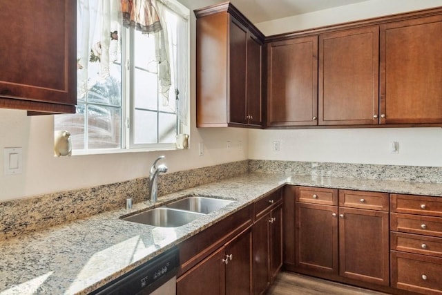 kitchen with sink, stainless steel dishwasher, light stone counters, and light wood-type flooring