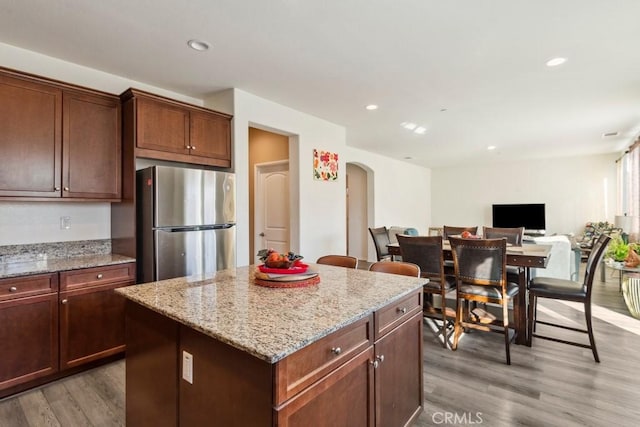 kitchen featuring a kitchen island, hardwood / wood-style floors, stainless steel fridge, and light stone counters