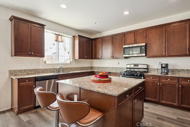 kitchen with sink, a center island, stainless steel appliances, light stone countertops, and light hardwood / wood-style flooring