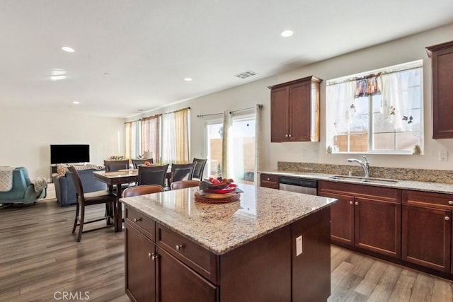 kitchen with sink, wood-type flooring, light stone countertops, a kitchen island, and stainless steel dishwasher