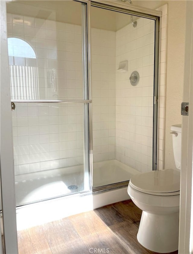 bathroom with hardwood / wood-style floors, toilet, and a shower with door