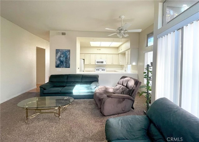 carpeted living room featuring a sink, visible vents, a skylight, and a ceiling fan
