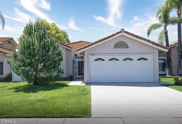 mediterranean / spanish-style home with a tiled roof, stucco siding, a front yard, an attached garage, and concrete driveway