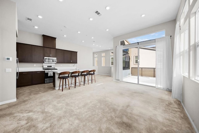 kitchen with light colored carpet, stainless steel appliances, a kitchen bar, and an island with sink