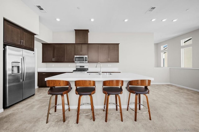 kitchen with light carpet, sink, an island with sink, and stainless steel appliances