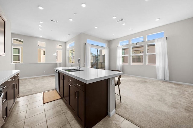 kitchen featuring a kitchen bar, a kitchen island with sink, dark brown cabinets, light colored carpet, and sink