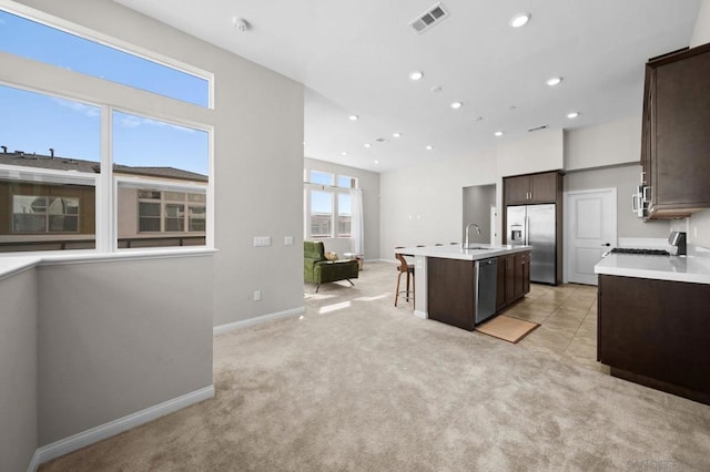 kitchen with a center island with sink, stainless steel appliances, a kitchen breakfast bar, dark brown cabinets, and sink