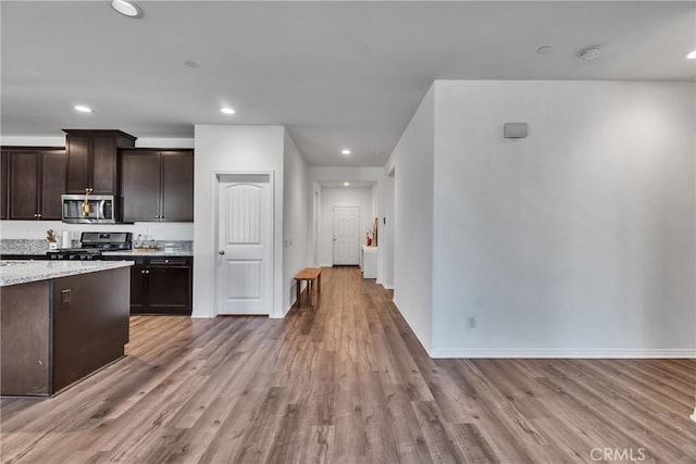 kitchen featuring light stone countertops, appliances with stainless steel finishes, dark brown cabinets, and light hardwood / wood-style floors