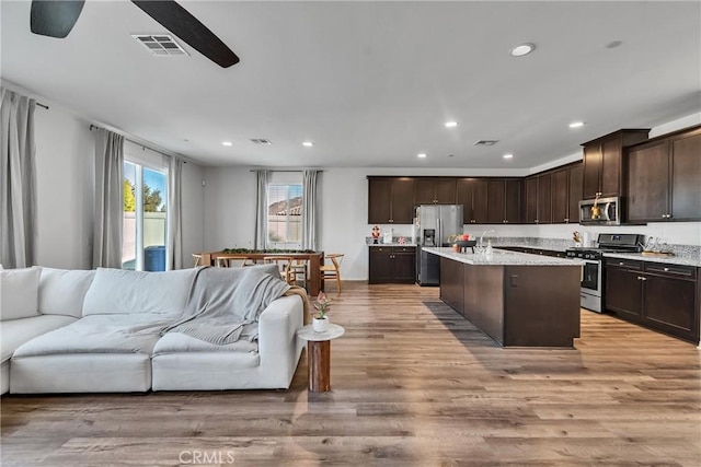 kitchen with light hardwood / wood-style floors, ceiling fan, stainless steel appliances, a kitchen island with sink, and dark brown cabinetry