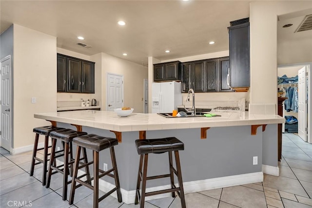 kitchen featuring a kitchen bar, sink, light tile patterned flooring, white refrigerator with ice dispenser, and tile counters