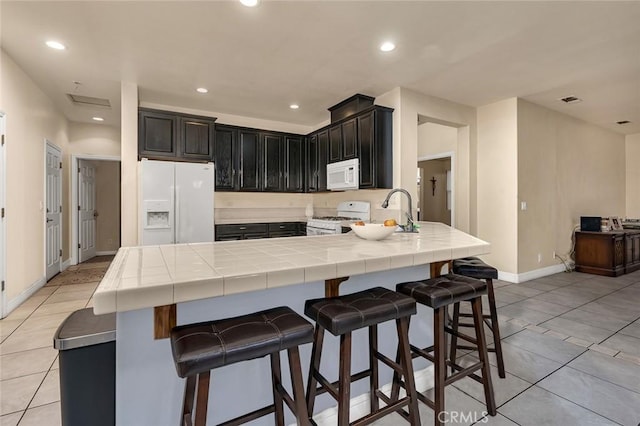 kitchen with white appliances, sink, tile countertops, light tile patterned floors, and a breakfast bar area